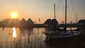 Tyyni järvi, jossa on veneitä, purjevene ja taustalla näkyviä taloja auringonlaskun aikaan.