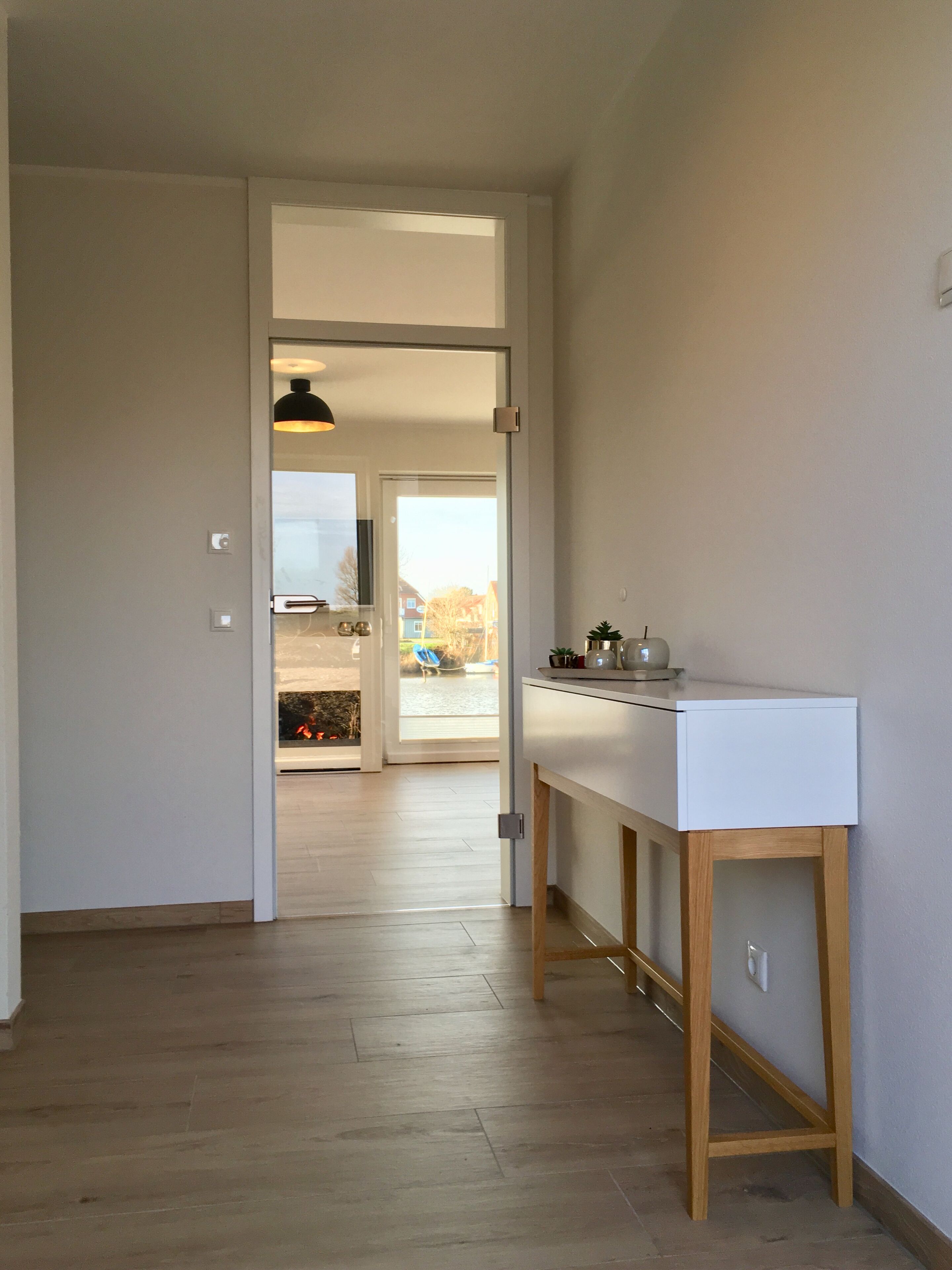 A hallway with a wooden floor leading to a kitchen area with a white countertop and a hanging pendant light.
