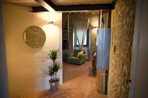 Un couloir avec une plante en pot, un élément décoratif rond fixé au mur, un canapé vert et un mur en pierre.