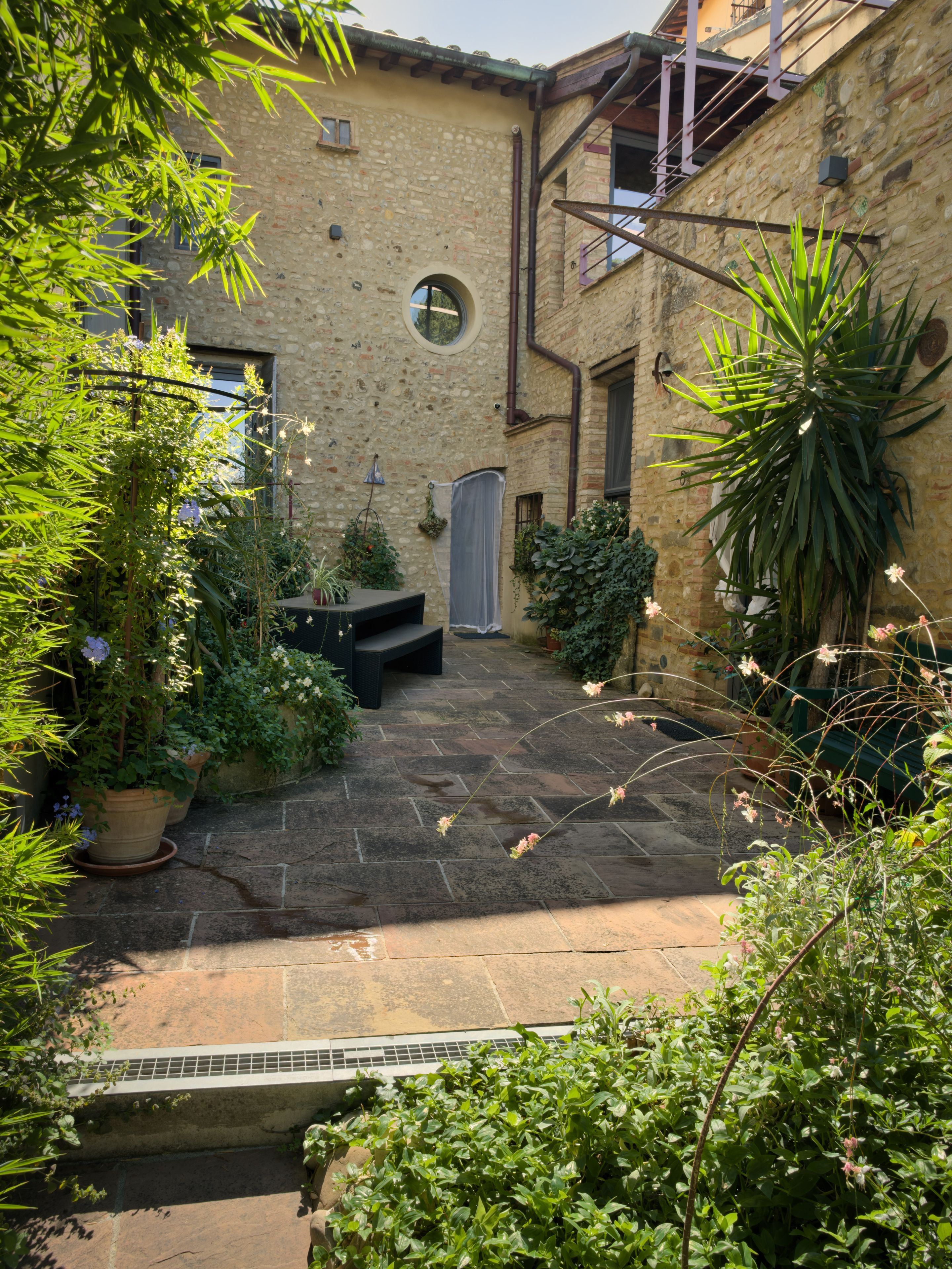 A courtyard with stone flooring, potted plants, and a small seating area.
