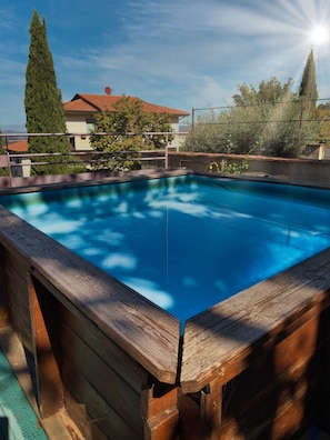 Ein rechteckiger Swimmingpool mit Holzbrücke, umgeben von einem Metallzaun, und ein klarer Himmel darüber.