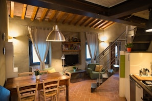 Un salon chaleureux avec une table à manger en bois, des chaises, un téléviseur et un escalier menant à un niveau supérieur.