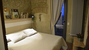 A bedroom with a bed, a stone wall, a window with curtains, and a small table with a plant. - Locanda del podestà: 17th century mansion in Chianti (Montespertoli)