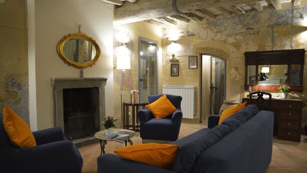 A living room with a fireplace, blue sofas with orange cushions, a round mirror, and a wooden cabinet. - Locanda del podestà: 17th century mansion in Chianti (Montespertoli)