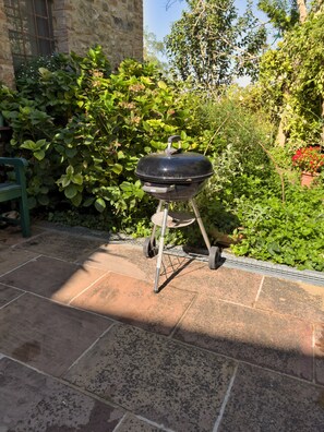 Un barbecue dans un jardin avec des murs en pierre et de la verdure.