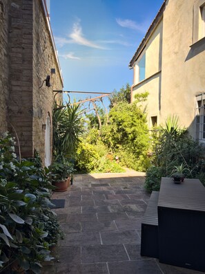 A courtyard with stone paving, potted plants, and a pergola.