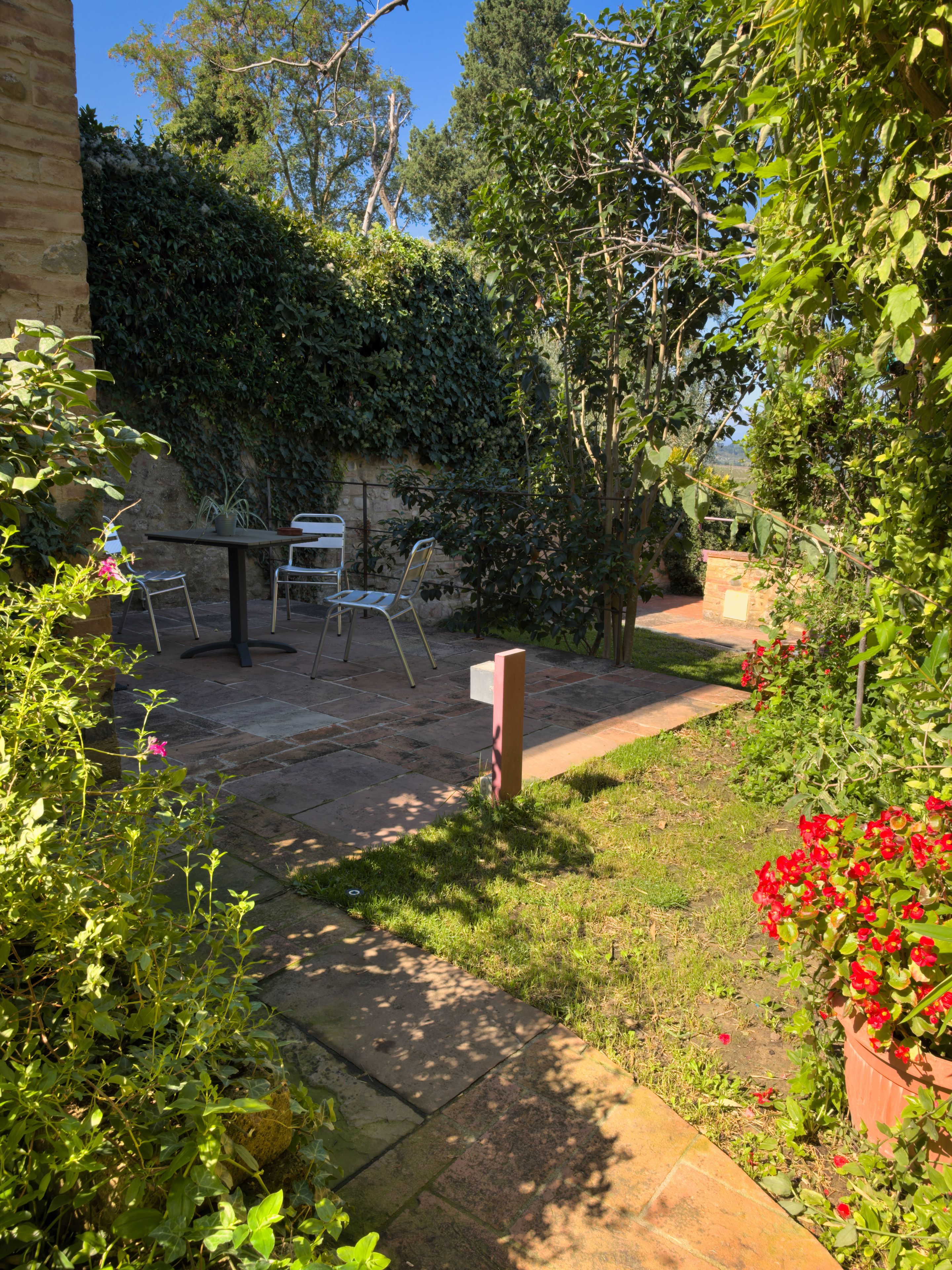 A patio with a table and chairs, surrounded by greenery and a stone wall.