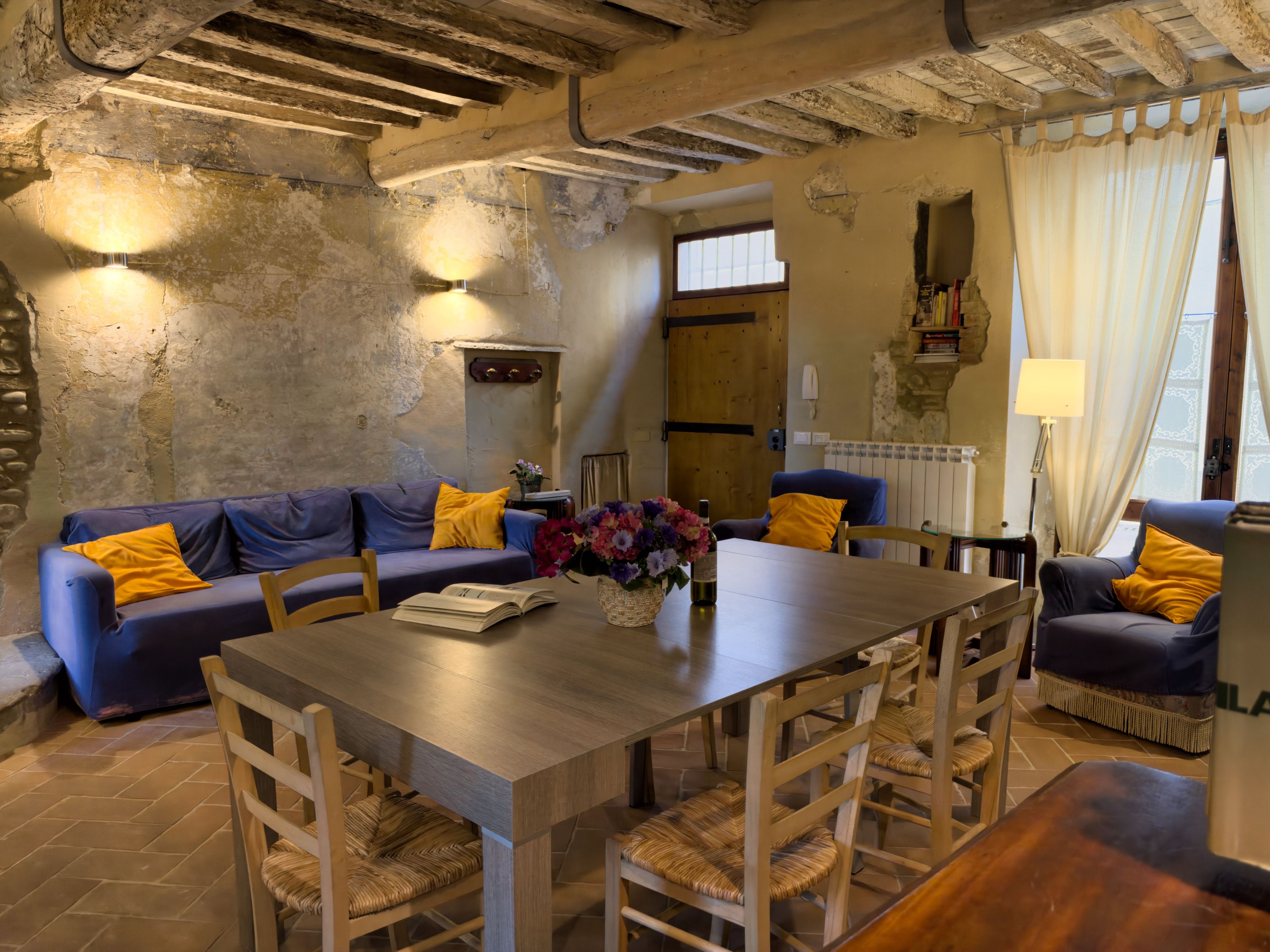 A rustic interior with a wooden dining table, blue sofa, and wicker chairs.