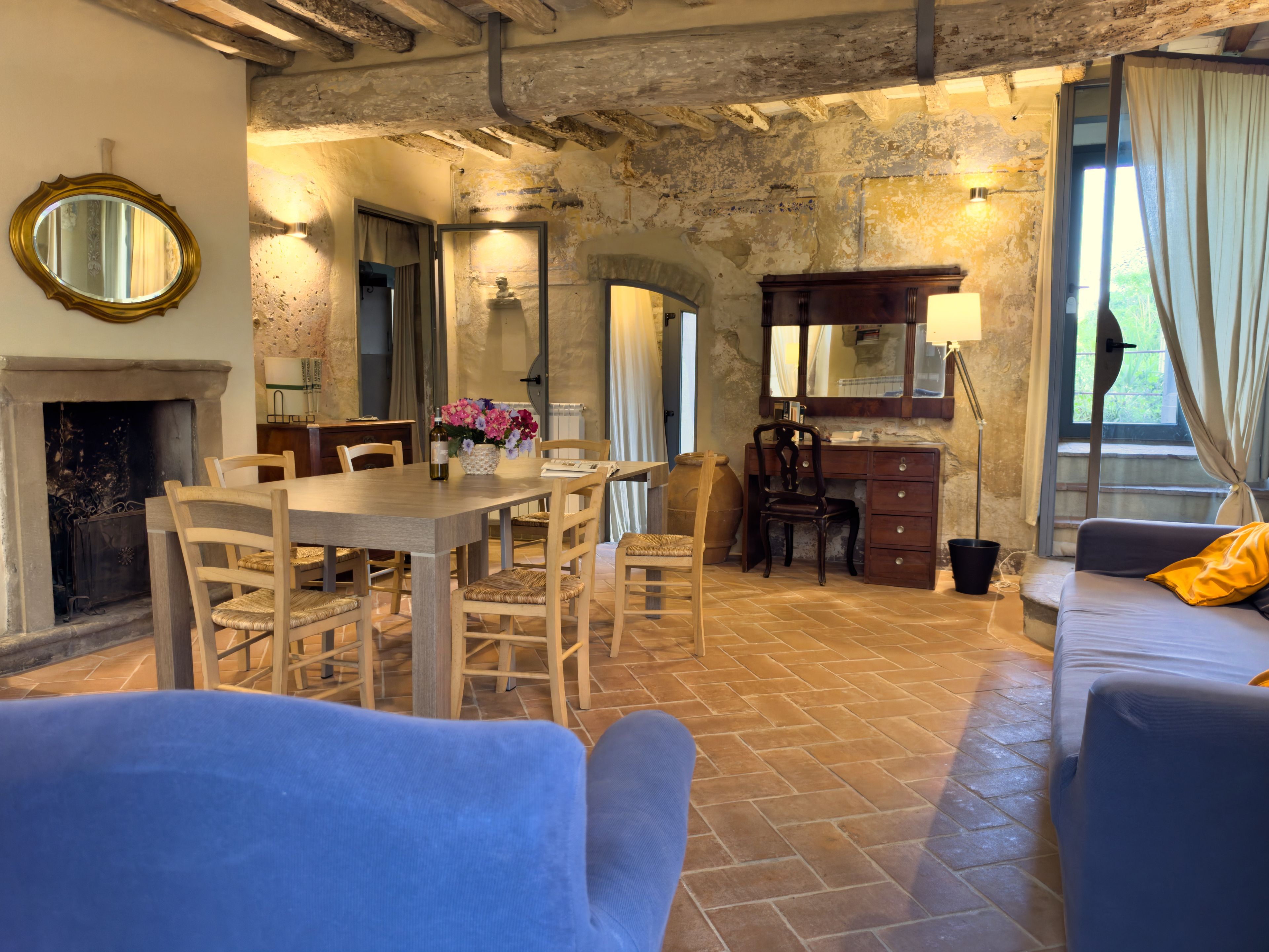 A rustic room with a dining table, chairs, a sofa, a fireplace, and a stone wall.