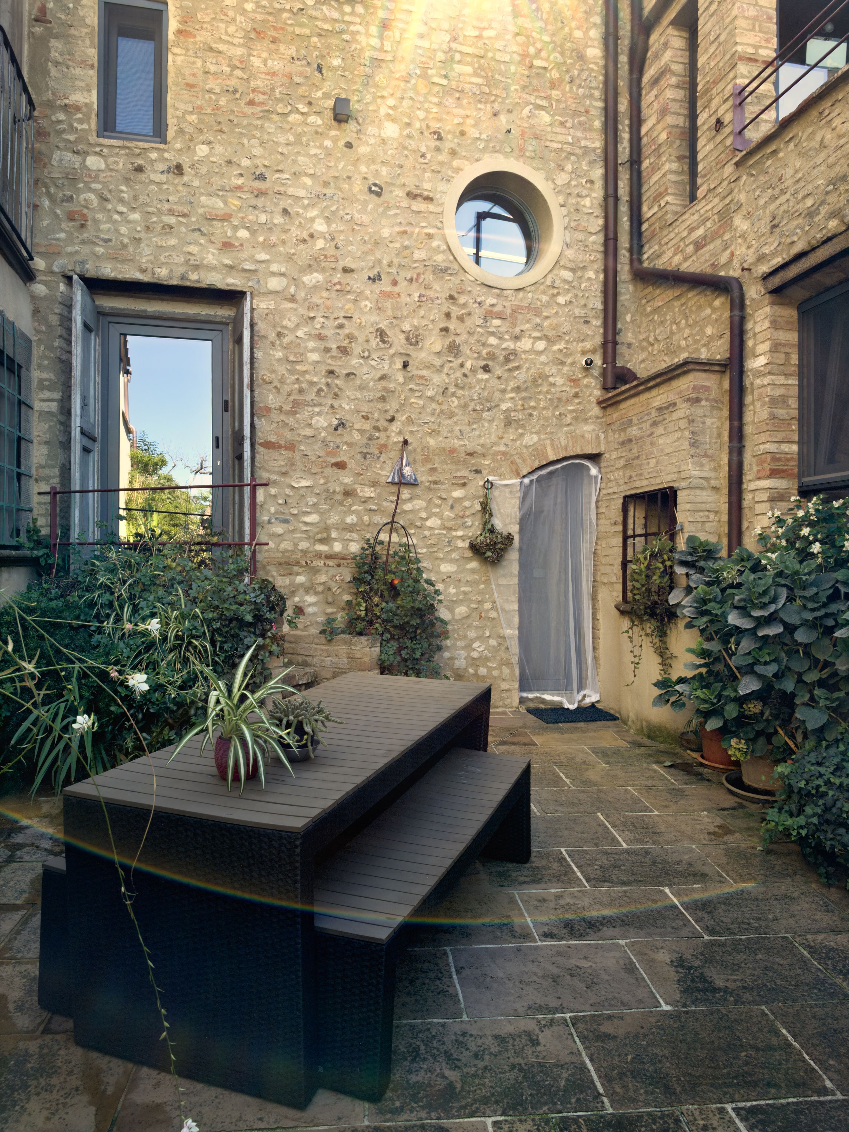 Une cour avec un banc en bois, des plantes en pot et un mur de pierre.