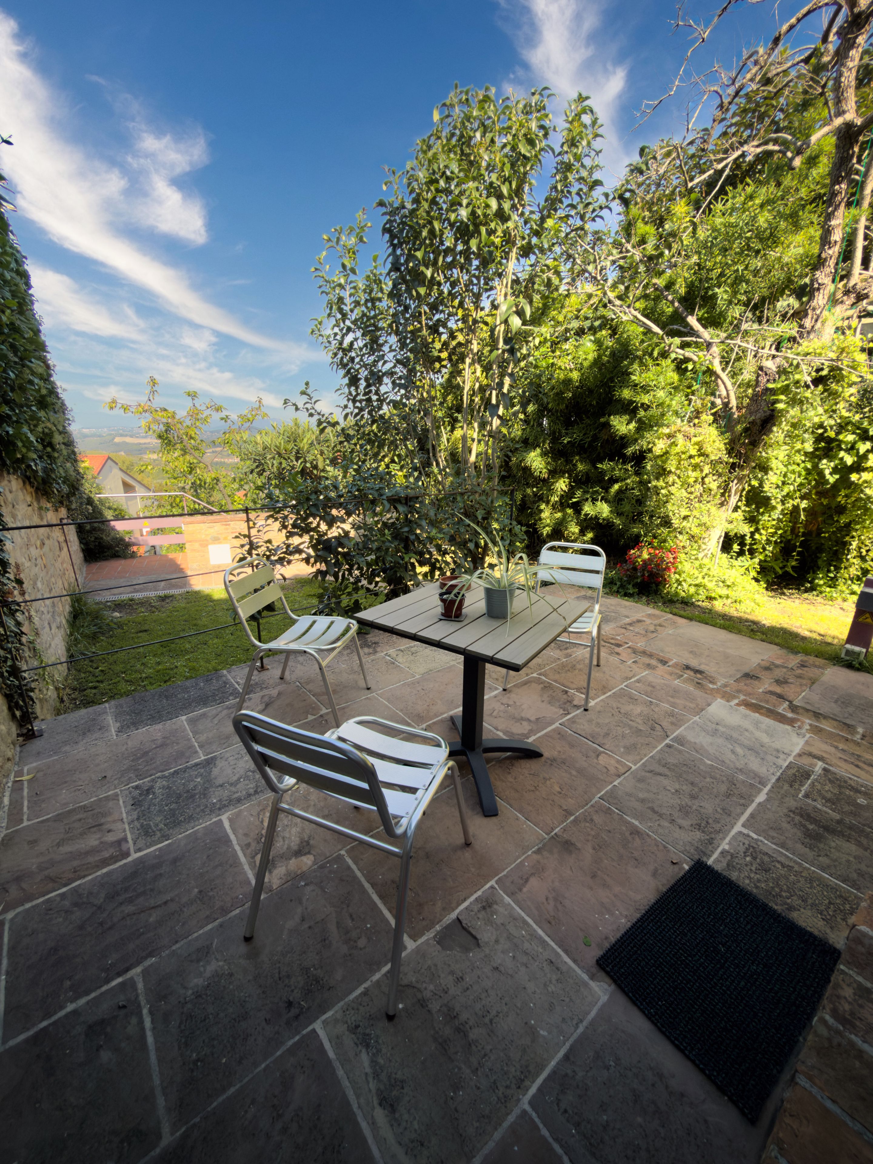 An outdoor patio with a table and chairs, surrounded by greenery and a view of the landscape.