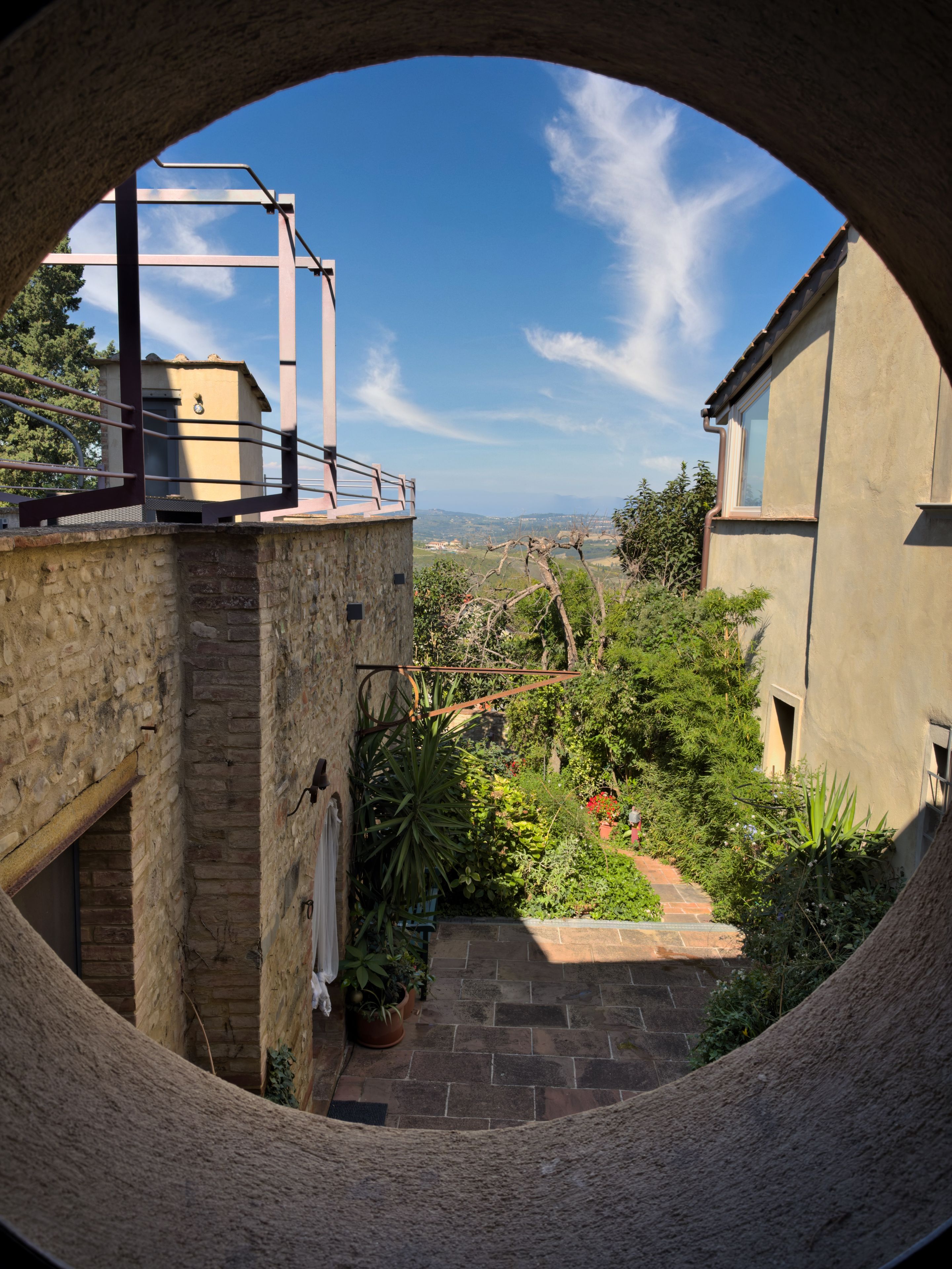 A circular view of a courtyard with a stone wall, a metal railing, and a potted plant.