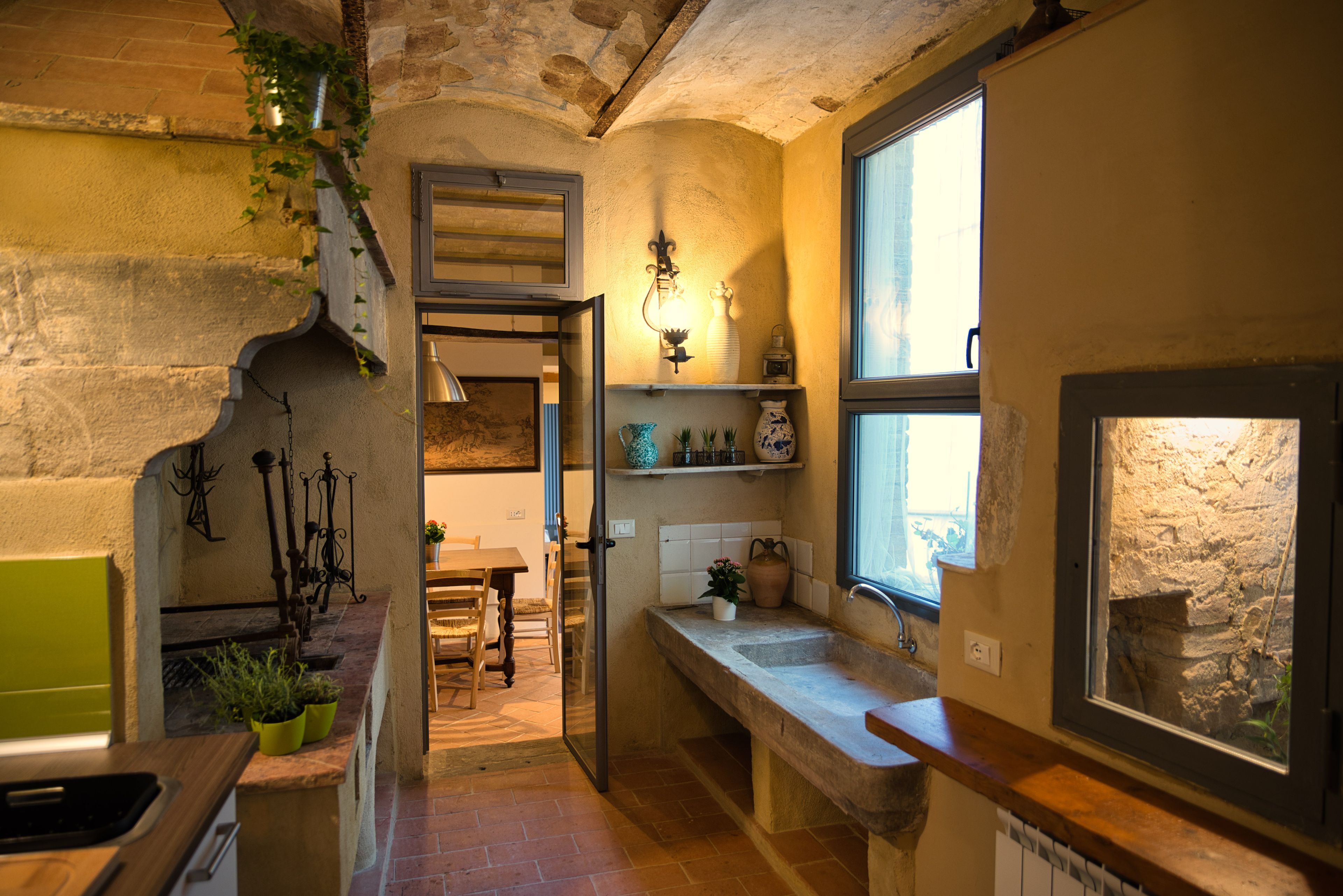 A rustic kitchen with a stone wall, a wooden counter, and a window overlooking a garden.