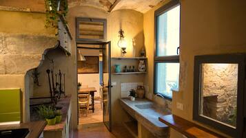 A rustic kitchen with a stone wall, a wooden counter, and a window overlooking a garden.