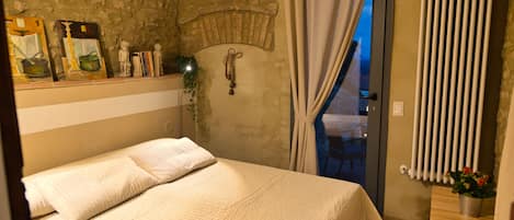 A bedroom with a bed, a stone wall, a window with curtains, and a radiator.