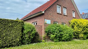 A red-brick house with a sloped roof, surrounded by green hedges and a paved lawn. - Ferienhaus Seehund on the East Frisian North Sea coast with 3 bedrooms (Hamswehrum)