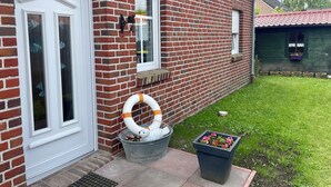A brick house with a white door, a window with a bell, and a garden with a flower pot. - Ferienhaus Seehund on the East Frisian North Sea coast with 3 bedrooms (Hamswehrum)