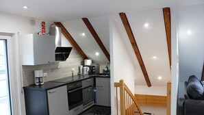 A compact kitchen with modern appliances, a wooden staircase, and a cozy seating area.