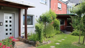 A residential property with a paved garden path, a small patio area with outdoor furniture, and a variety of plants and flowers.