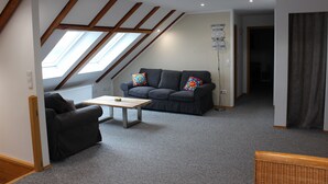 A room with a sloped ceiling, a sofa, a chair, a small table, and a floor lamp.
