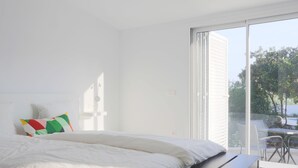 Un dormitorio con cama, almohada colorida y vistas al exterior a través de un ventanal corredero.
