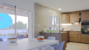 Una cocina moderna con armarios de madera, encimera blanca y comedor con mesa blanca y sillas azules.