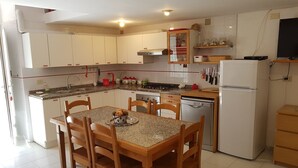 A compact kitchen with white cabinets, a granite countertop, a dining table with chairs, and a built-in dishwasher.