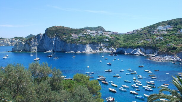 A coastal town with boats anchored in the bay, surrounded by cliffs and greenery.