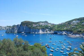 A coastal town with boats anchored in the bay, surrounded by cliffs and greenery.