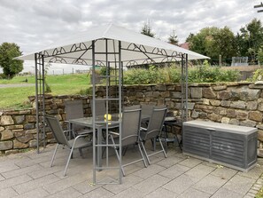 An outdoor patio with a covered table and chairs, stone wall, and a view of the surrounding landscape. - Bright, beautiful double room with a wide view in a quiet location (Borler)