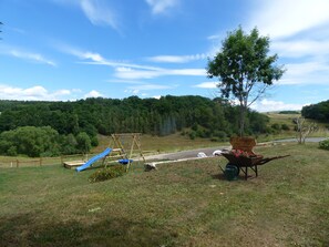 A playground with a slide and swings, surrounded by a grassy field and a forested hill. - Bright, beautiful double room with a wide view in a quiet location (Borler)