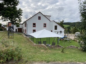 A white building with red window frames, a covered outdoor area, and a playground with a slide. - Bright, beautiful double room with a wide view in a quiet location (Borler)