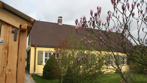 A yellow house with a brown tiled roof, a wooden door, and a small garden with blooming pink flowers. - beautiful garden with village idyll on the lagoon (usedom)