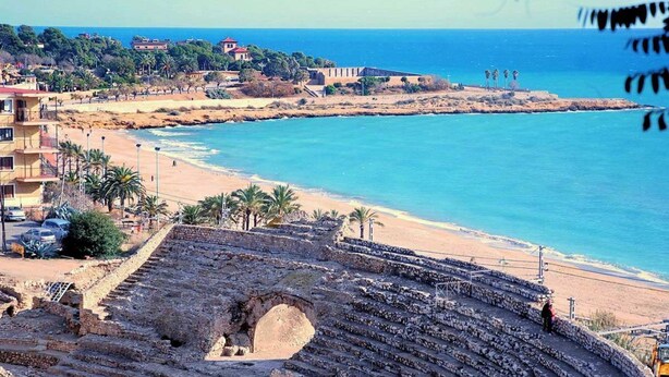 Ein uraltes Amphitheater mit Steinstufen und einer zentralen Bühne, das auf einen Strand und das Meer blickt.