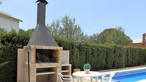 Ein Außenbereich mit Grill, einer Ziegelofen, einem Tisch mit Stühlen und einem Blumentopf.