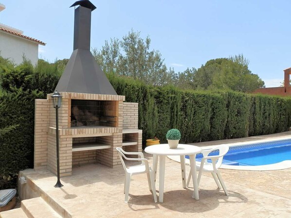 An outdoor barbecue area with a brick oven, a table with chairs, and a potted plant.