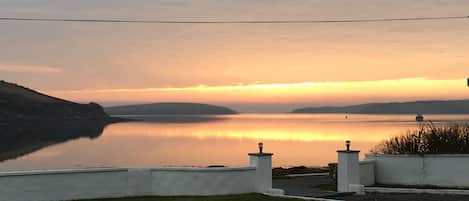 A serene lakeside view with a calm water body reflecting the sky, surrounded by grassy areas and a white fence.