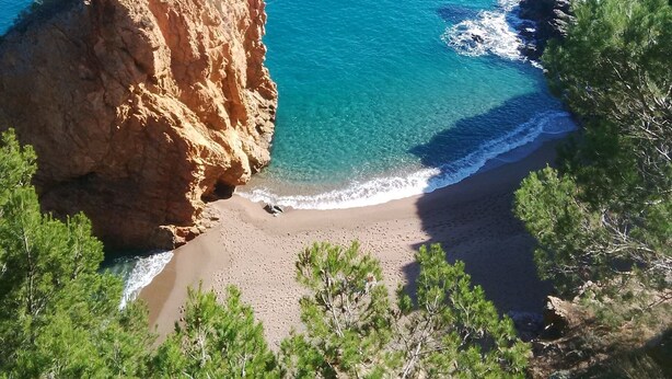 Un paisaje costero con un acantilado rocoso, mar azul cristalino y una playa de arena.
