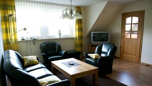 A living room with a sofa, two chairs, a coffee table, a television, and a window with curtains. - spacious apartment in the countryside, ideal starting point for cycling (Rosendahl)