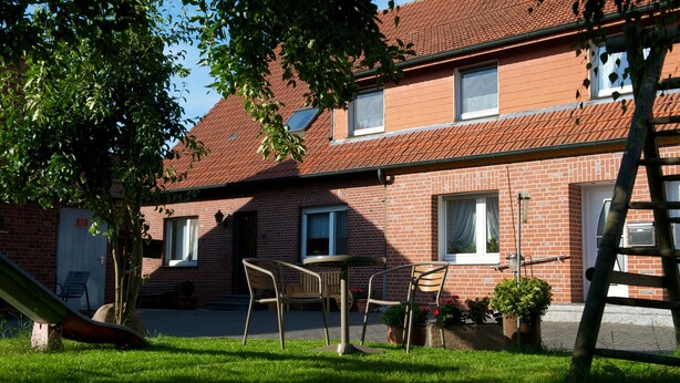 A brick building with a red-tiled roof, a small patio with a table and chairs, and a ladder leaning against the building. - spacious apartment in the countryside, ideal starting point for cycling (Rosendahl)