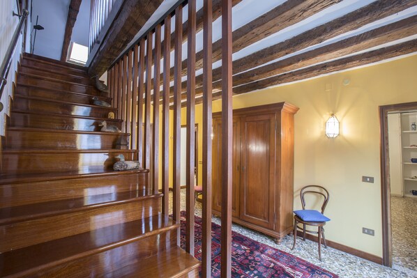 A wooden staircase with a red patterned carpet, a wooden chair with a blue cushion, and a wall-mounted light fixture.