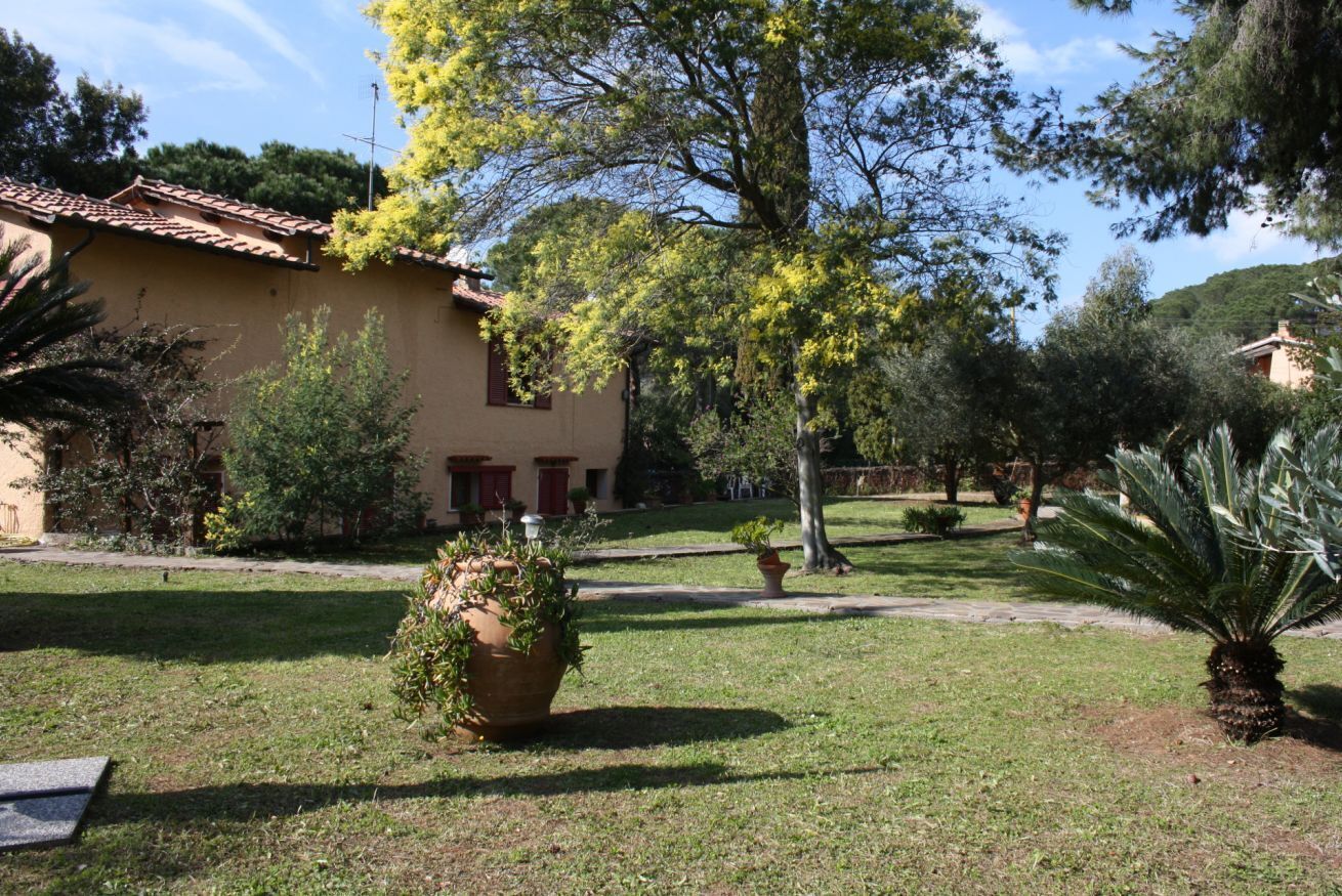 A building with a tiled roof, surrounded by a well-maintained garden with various plants and a palm tree.