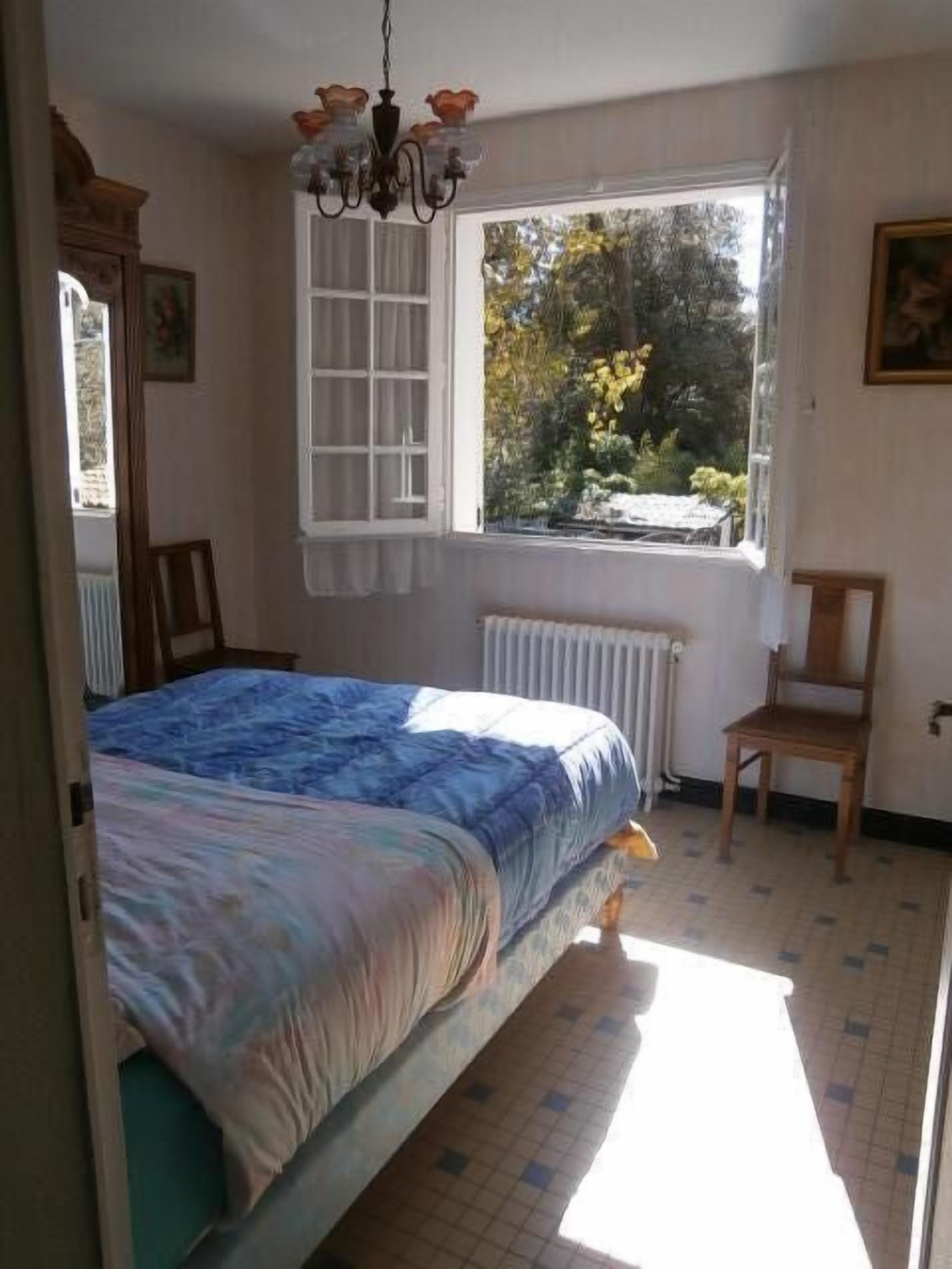 A bedroom with a bed, a window with a view of trees, a radiator, and a chair.