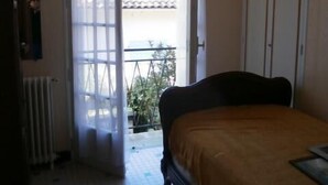 A bedroom with a bed, a radiator, a window with curtains, a chandelier, and a door leading to an outdoor area. - Spacious 3 bedroom villa near downtown, market and beaches (RONCE LES BAINS LA TREMBLADE)