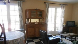A room with a checkered floor, a wooden cabinet, a television, a chair, and a table. - Spacious 3 bedroom villa near downtown, market and beaches (RONCE LES BAINS LA TREMBLADE)