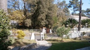 A stone pathway leading to a gated area with a small bridge, surrounded by trees and a grassy lawn. - Spacious 3 bedroom villa near downtown, market and beaches (RONCE LES BAINS LA TREMBLADE)