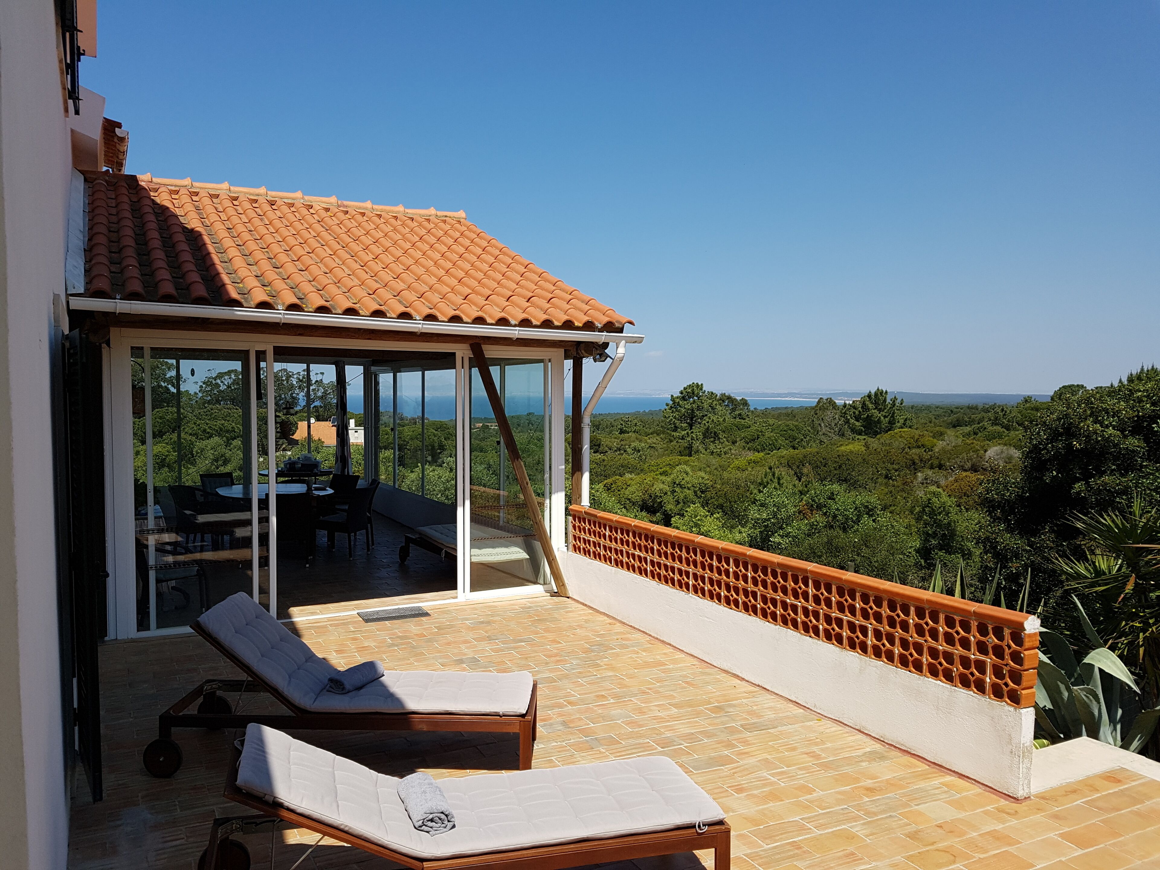 A terrace with two sun loungers, a glass door leading to an outdoor dining area, and a view of a lush landscape.