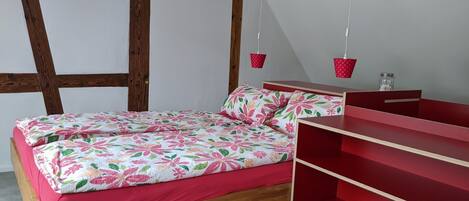 A bedroom with a wooden bed frame, a red nightstand, and a hanging light fixture.