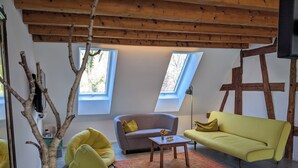 Un soggiorno moderno con soffitto alto, travi in legno, due lucernari, un divano giallo, un divano grigio e una poltrona sacco gialla.