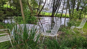 Un'area relax esterna tranquilla, con sedie in metallo e una panchina, immersa nel verde e con uno stagno.